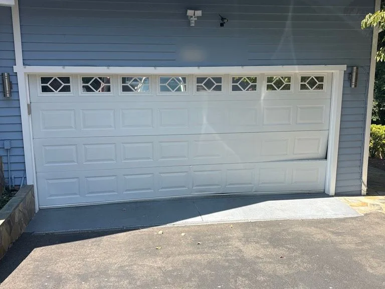 Damaged white garage door with bent panel on a blue Bellevue home